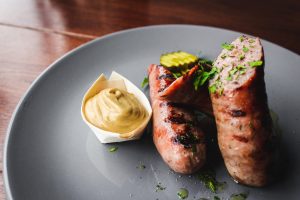 two sausages on a plate with mustard on the side